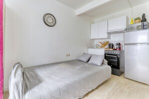 Een kleine kamer met een bed, kitchenette en een wandklok.