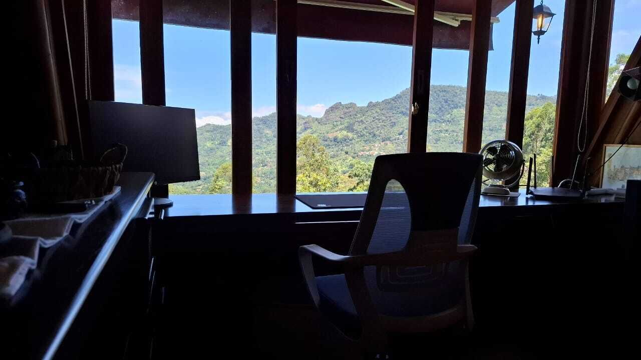 A room with a view of a mountainous landscape through large windows, a desk with a computer, and a chair.