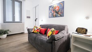 Una sala de estar moderna con un sofá gris, cojines coloridos, un bolso estampado con diseño de cebra y un cuadro en la pared.