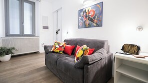 Ein modernes Wohnzimmer mit einem grauen Sofa, bunten Kissen, einer Tasche mit ZEBRA-Muster und einem Bild an der Wand.