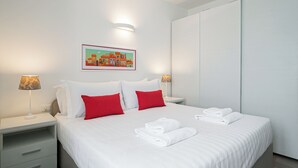 Habitación de hotel con cama, dos mesitas de noche, lámpara de pared y un cuadro enmarcado.