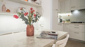 Cuina moderna amb armaris blancs, una campana extractora d'acer inoxidable i zona de dinar amb taula de marbre.