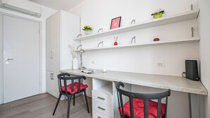 Cozinha moderna com armários brancos, bancada, duas cadeiras com almofadas vermelhas e uma prateleira com objetos decorativos.