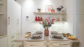 Uma cozinha moderna com armários brancos, uma mesa de jantar posta com pratos, copos e um vaso de flores.