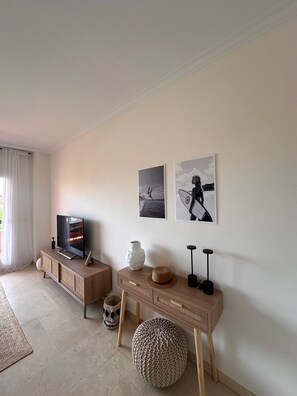 A living room with a television, a wooden console table, a woven pouf, and two wall-mounted picture frames. - Your peaceful retreat... Mi Casa del Sol in Casarès, with a pool just 1.3 km from the sea! (Casares)