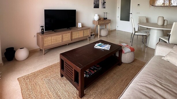 Ein Wohnzimmer mit Fernseher, Sofa, Couchtisch und einer Pendelleuchte.