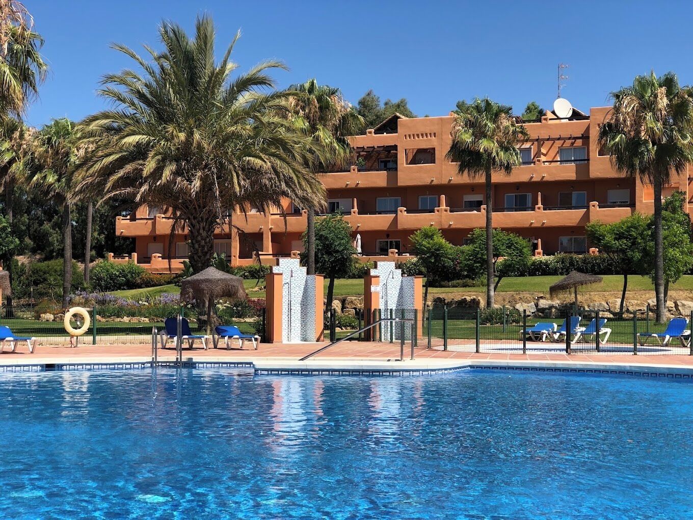 Ein Hotel mit Swimmingpool, Palmen und wolkenlosem, blauem Himmel.