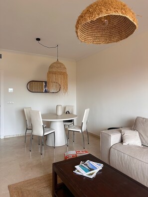 Ein modernes Wohnzimmer mit einem runden Esstisch, weißen Stühlen, einem dunklen Couchtisch und einem beigen Sofa.