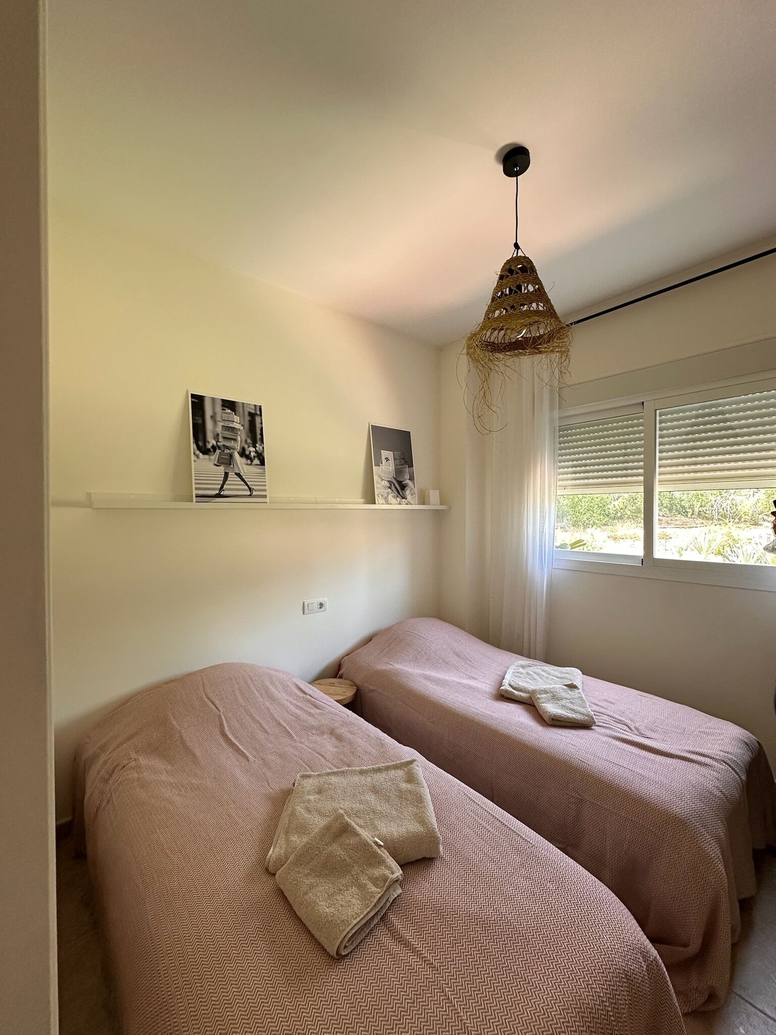 Una camera da letto con due letti, una lampada a sospensione e una finestra con persiane.