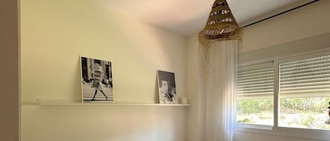Et soveværelse med to senge, en loftslampe og et vindue med persienner.