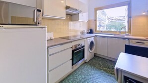 Eine kompakte Küche mit Mikrowelle, Backofen, Waschmaschine und einem Fenster mit Blick auf die Stadt.