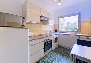 Cozinha compacta com micro-ondas, forno, máquina de lavar e janela com vista para a cidade.