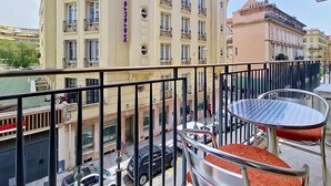 Ein Balkon mit Metallgeländer, einem Glastisch und roten Sitzmöbeln mit Kissen.