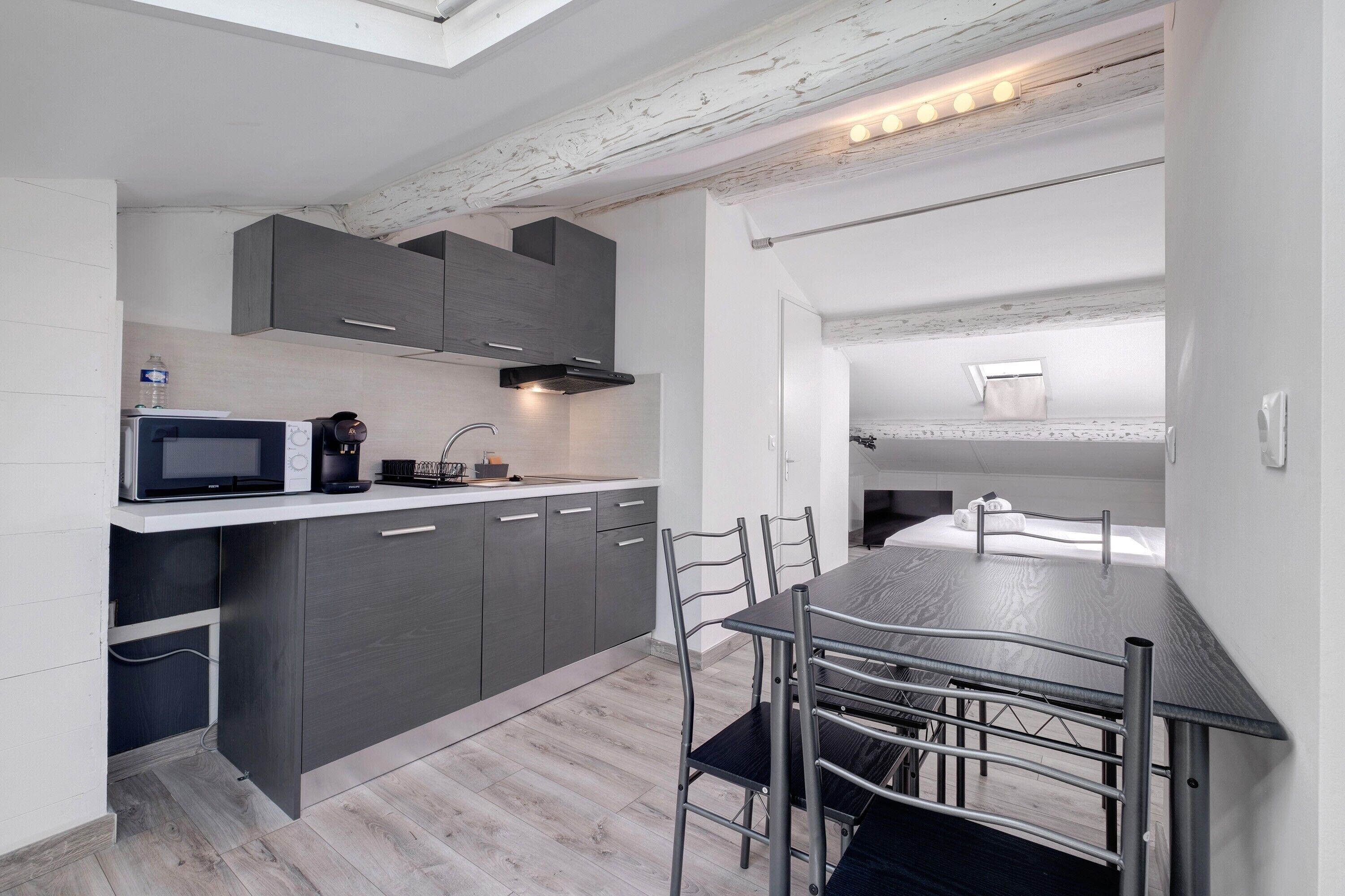 A compact kitchen with modern appliances, a dining area with metal chairs, and a loft bedroom with a skylight.