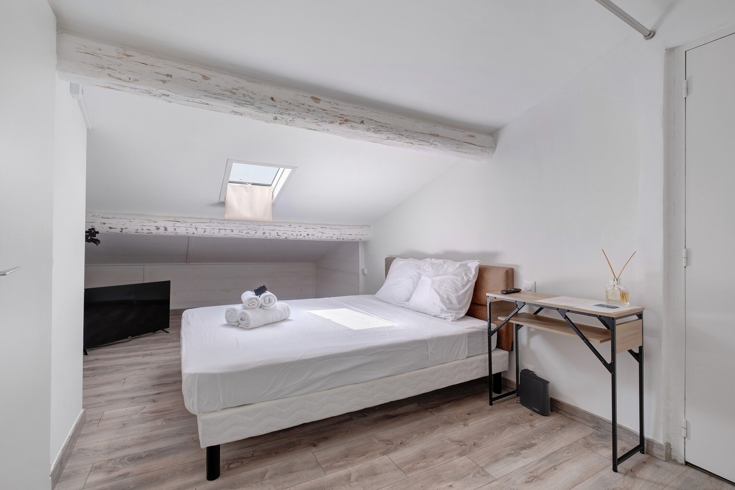 A bedroom with a bed, a desk, and a skylight.