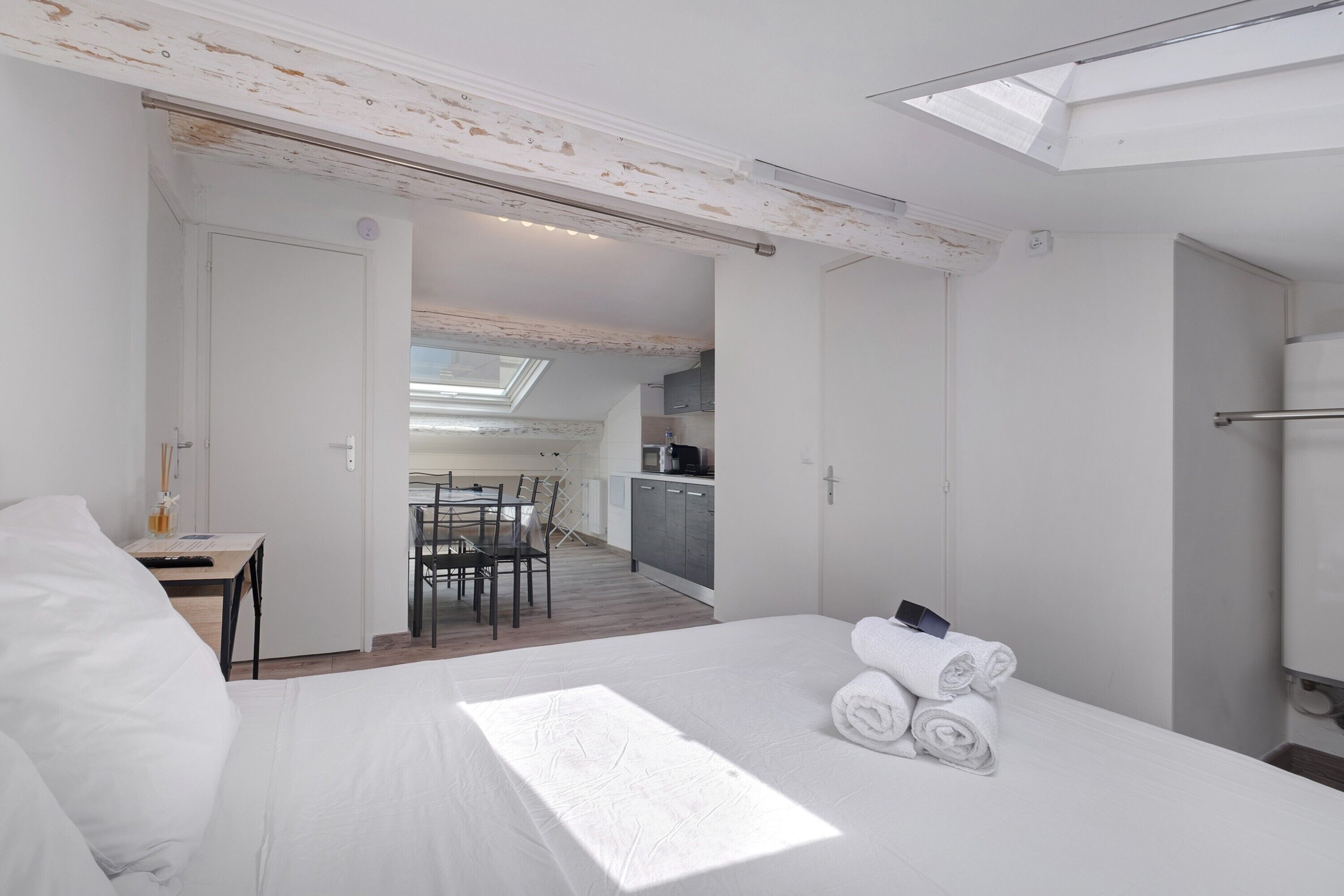 A hotel room with a bed, a desk, a chair, a bathroom, and a view of the kitchen and dining area.