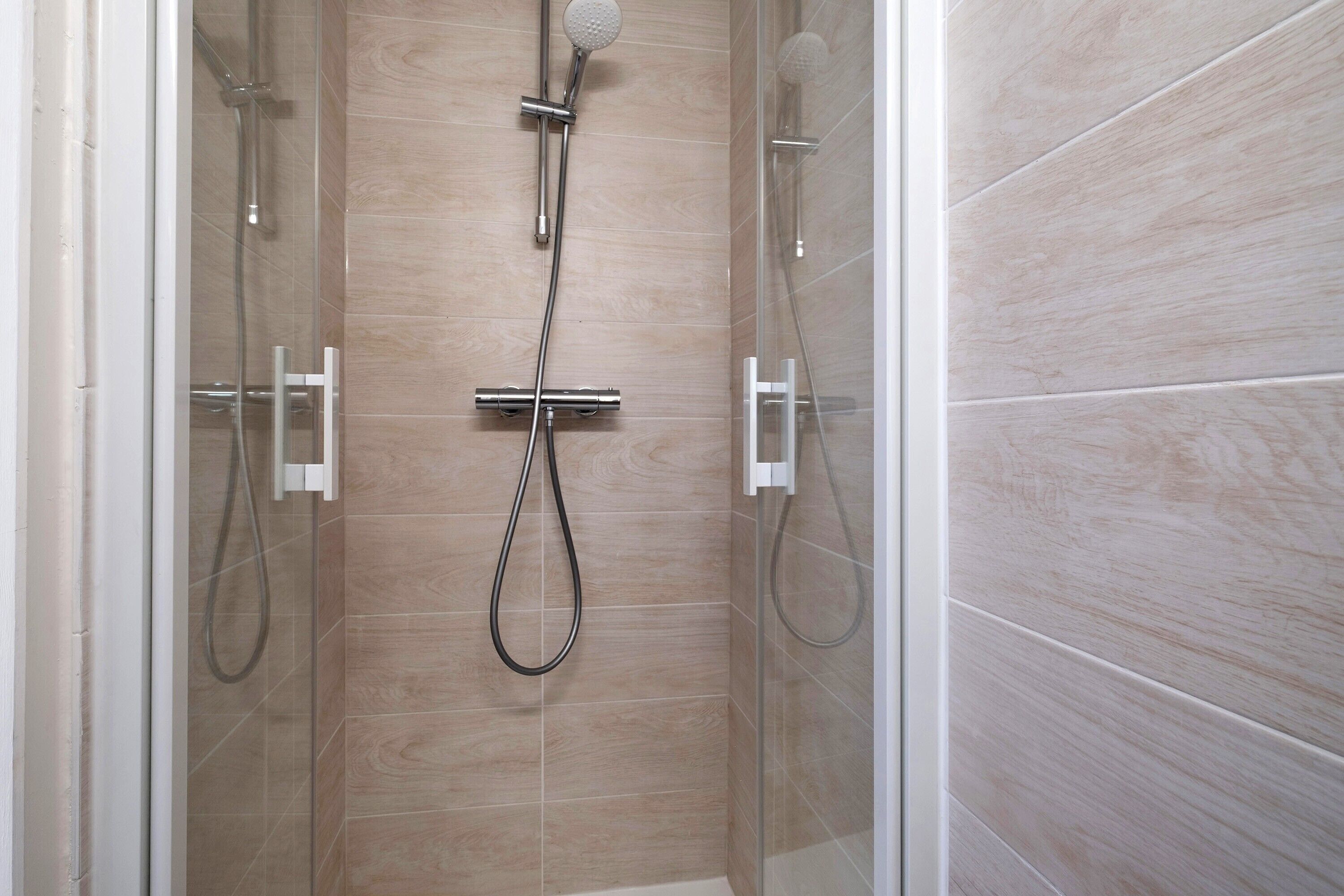 A glass-enclosed shower area with a handheld showerhead and a wall-mounted faucet.