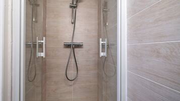 A glass-enclosed shower area with a handheld showerhead and a wall-mounted faucet.