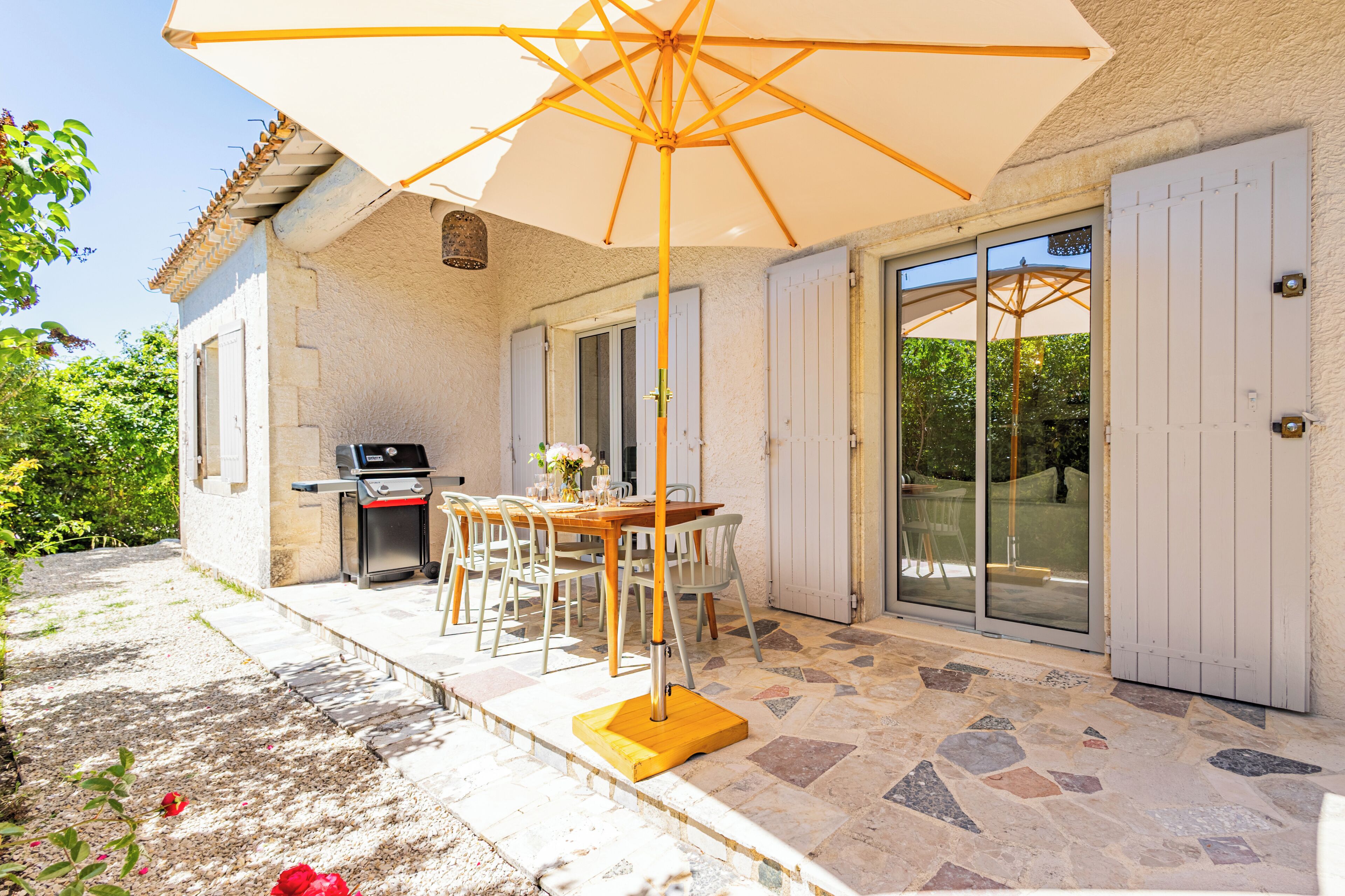 An outdoor patio with a table and chairs, a grill, and a large umbrella.