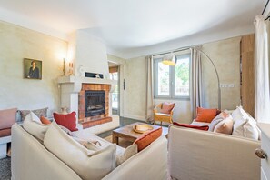 A living room with a fireplace, sofas, a coffee table, and a large window with curtains. - Villa Marius, fully renovated, walking distance to the village, A/C, pool (Saint-Rémy-de-Provence)