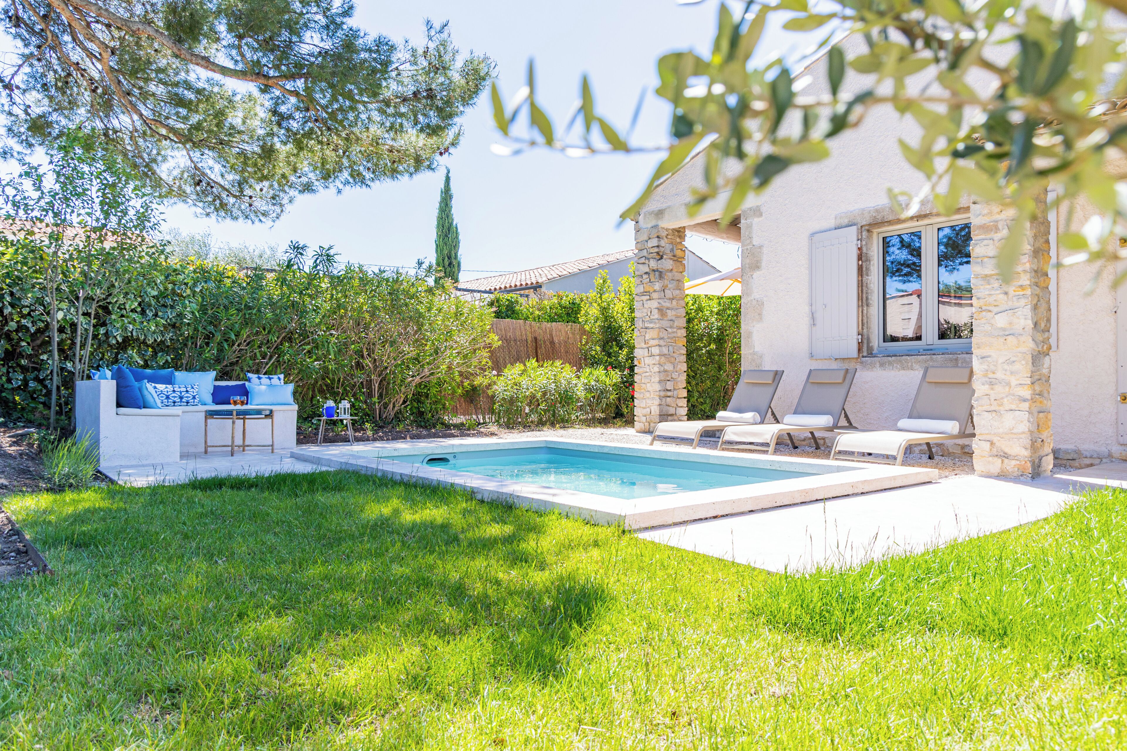 A swimming pool with lounge chairs, a stone pillar, and a white building with a window.