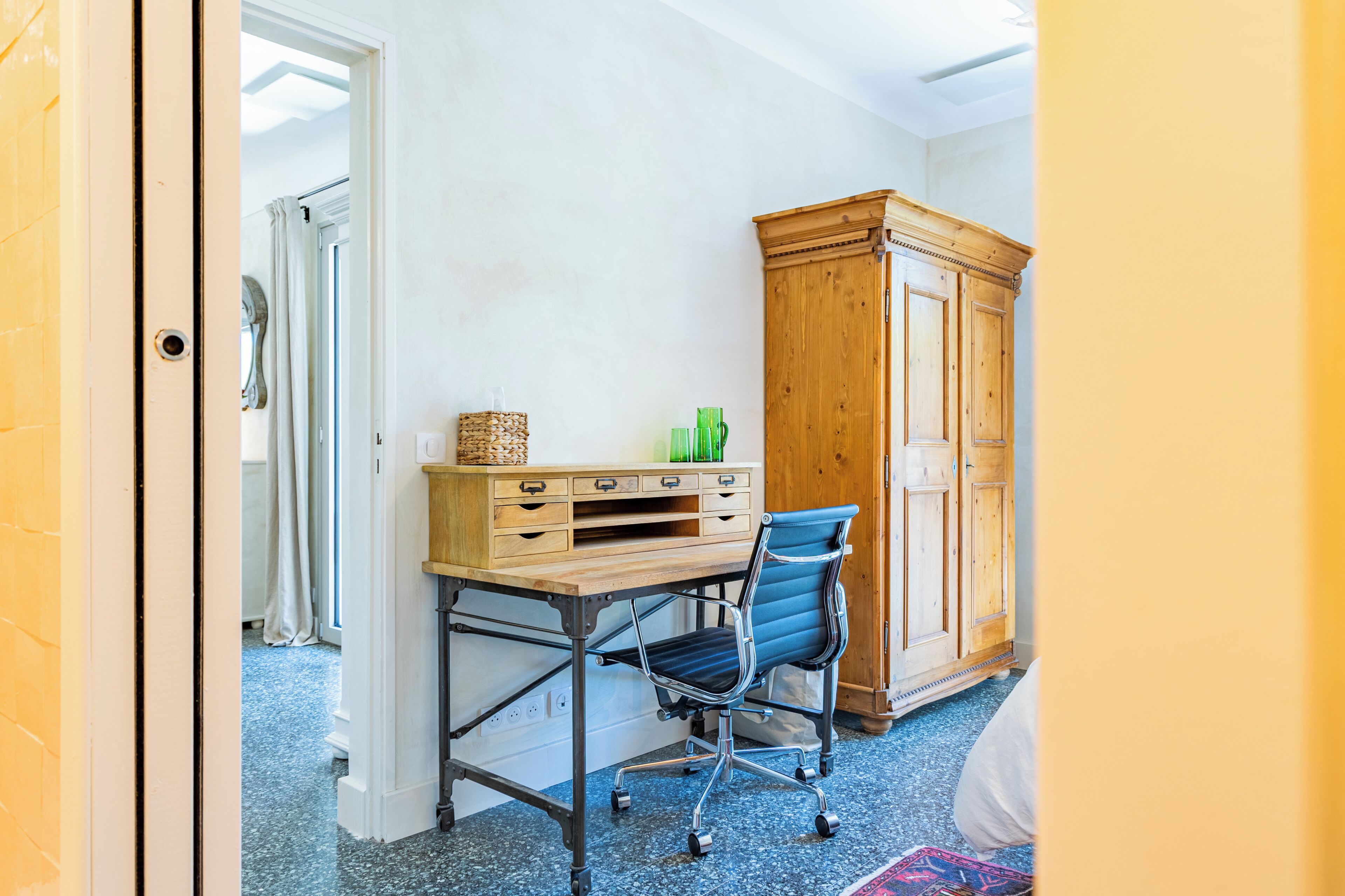 A room with a wooden desk, a blue office chair, a wooden wardrobe, and a patterned rug.