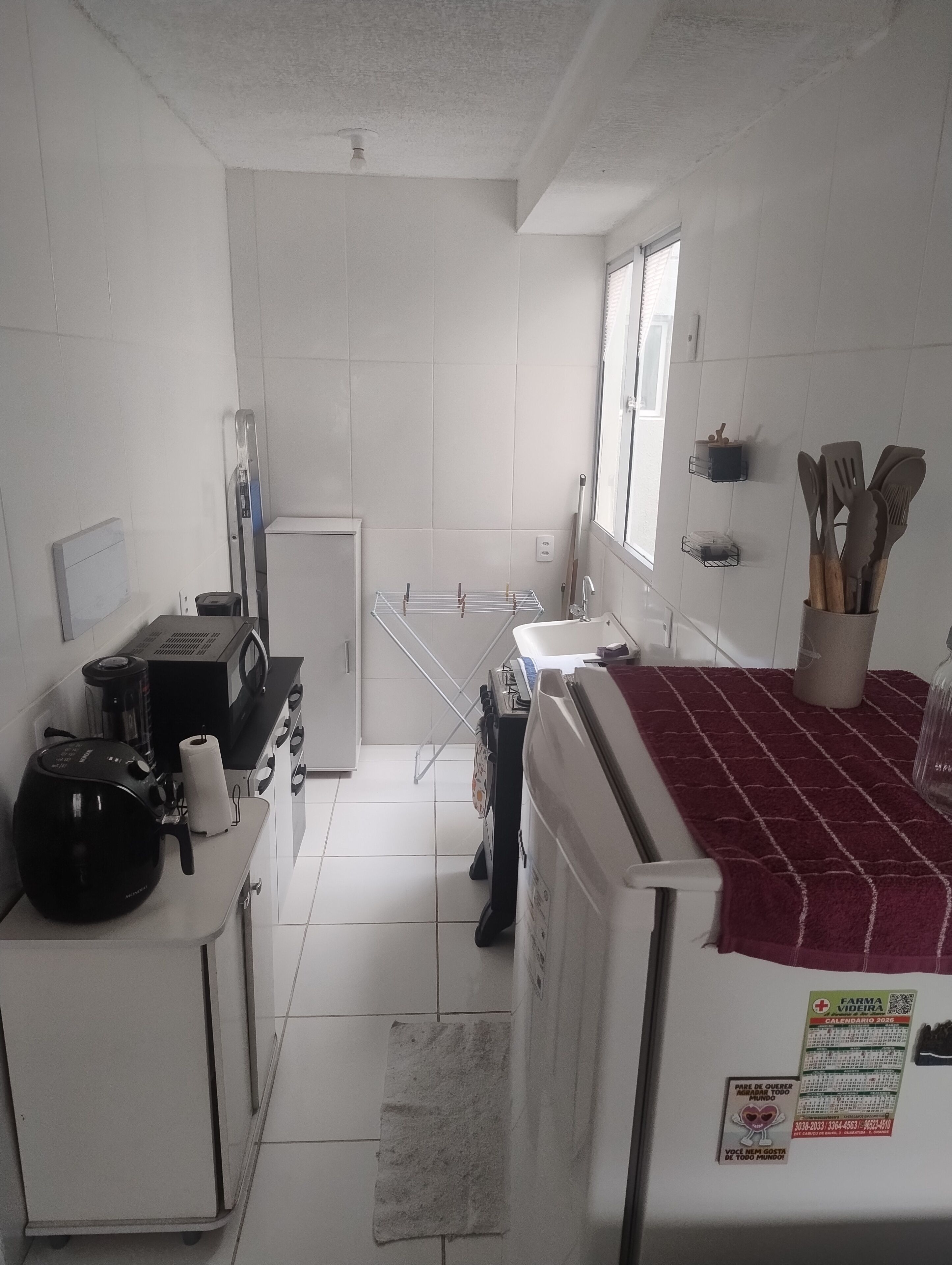 A compact kitchen with white tiles, a microwave, a coffee maker, and a refrigerator.