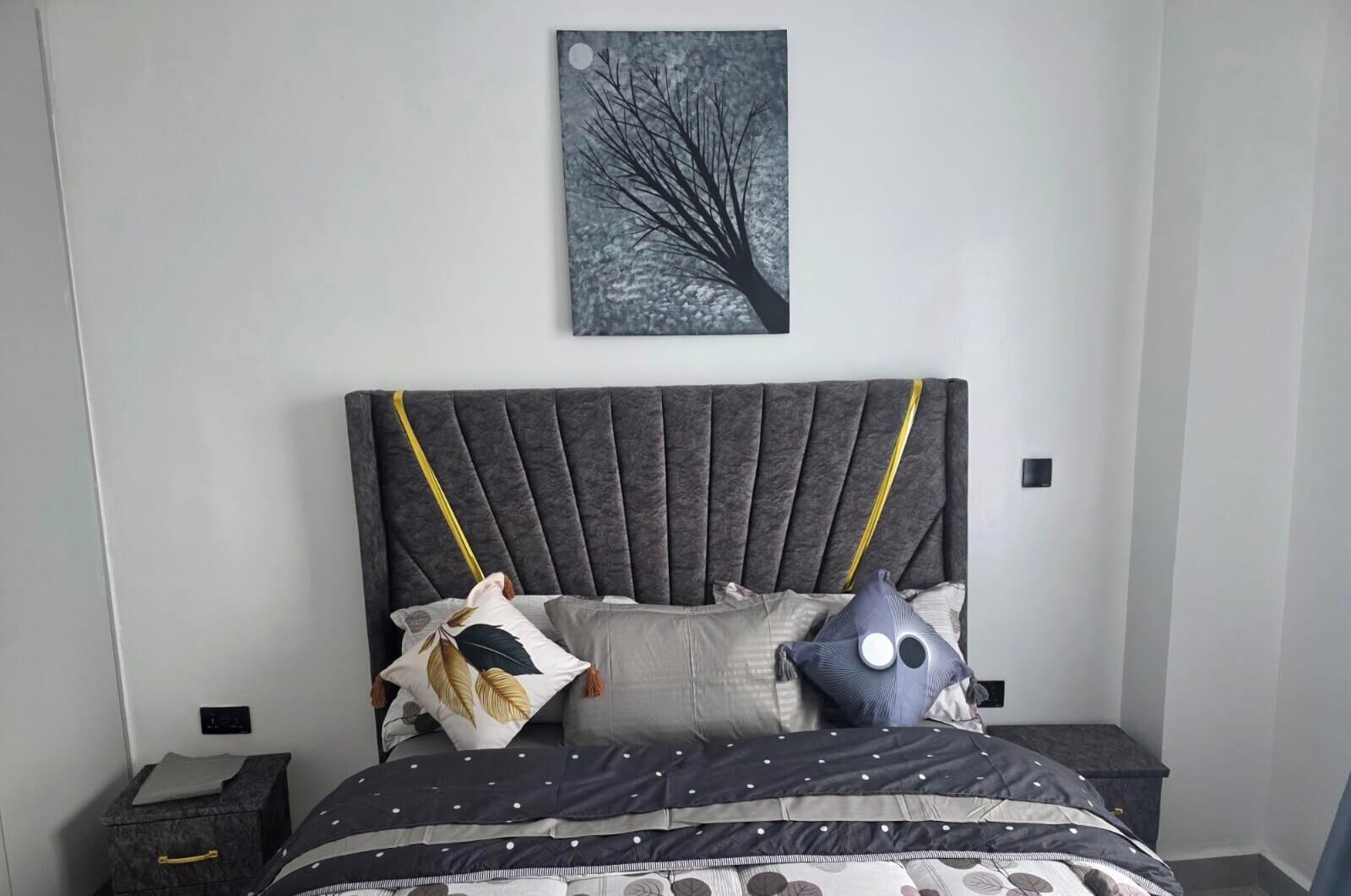 Ein Bett mit dunklem Kopfteil, mehreren Kissen und einer Steude mit Punkten.