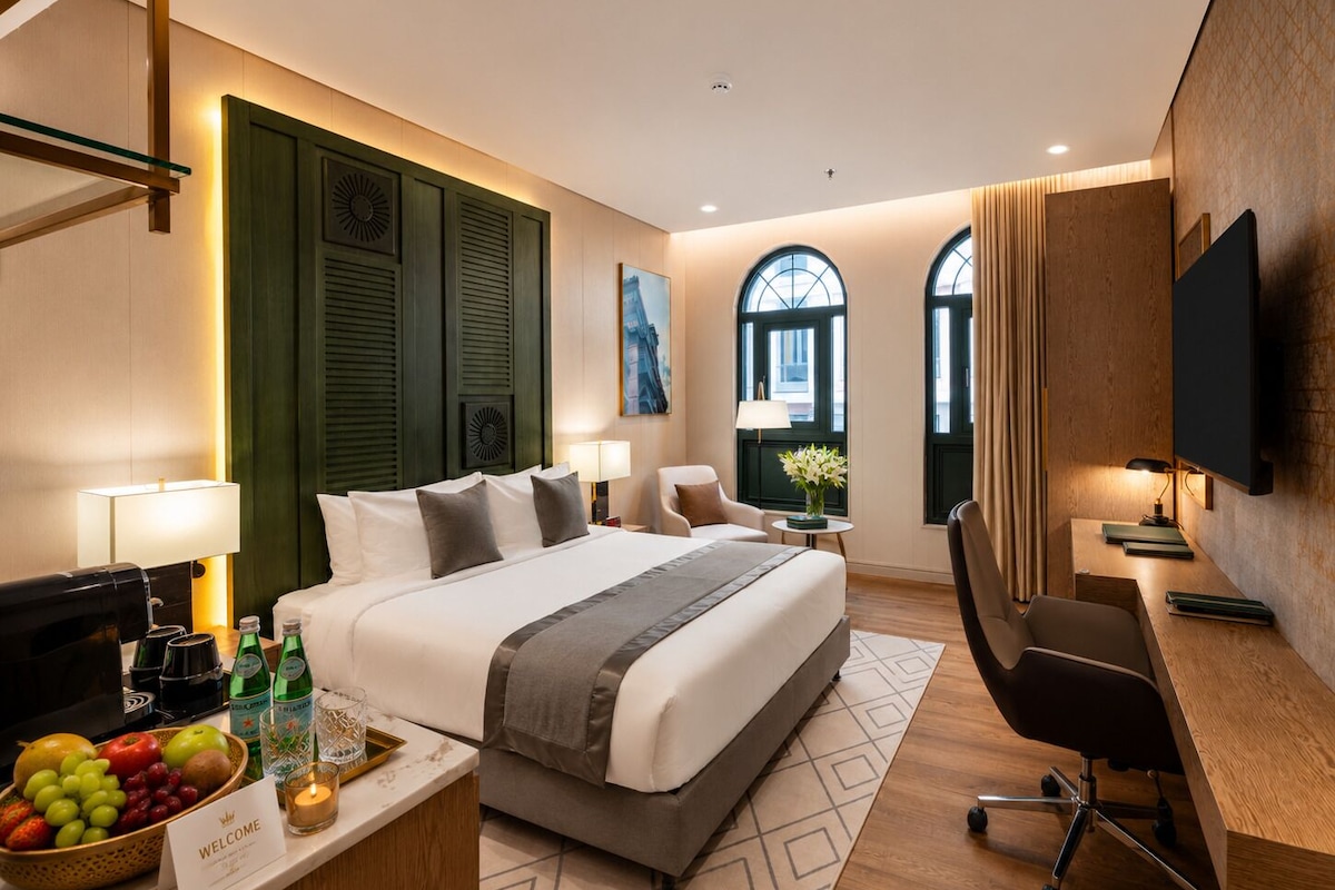 A hotel room with a large bed, a desk, a chair, a TV, and a window with curtains.