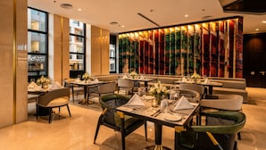 A modern dining area with tables set for service, a large window with a view, and a decorative wall with vertical elements. - Naviti By Warwick Jeddah (Al Quwaiiyah)