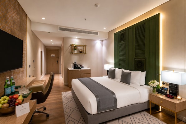 Habitación de hotel con cama, mesita de noche, televisor, escritorio y frutero.