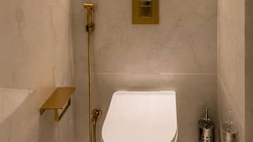 A modern bathroom with a white toilet, a gold showerhead, and a small shelf with a plant and a candle.