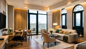 A modern hotel room with a large window, a sofa, a dining area, and a TV.