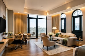 A modern hotel room with a large window, a sofa, a dining area, and a TV.