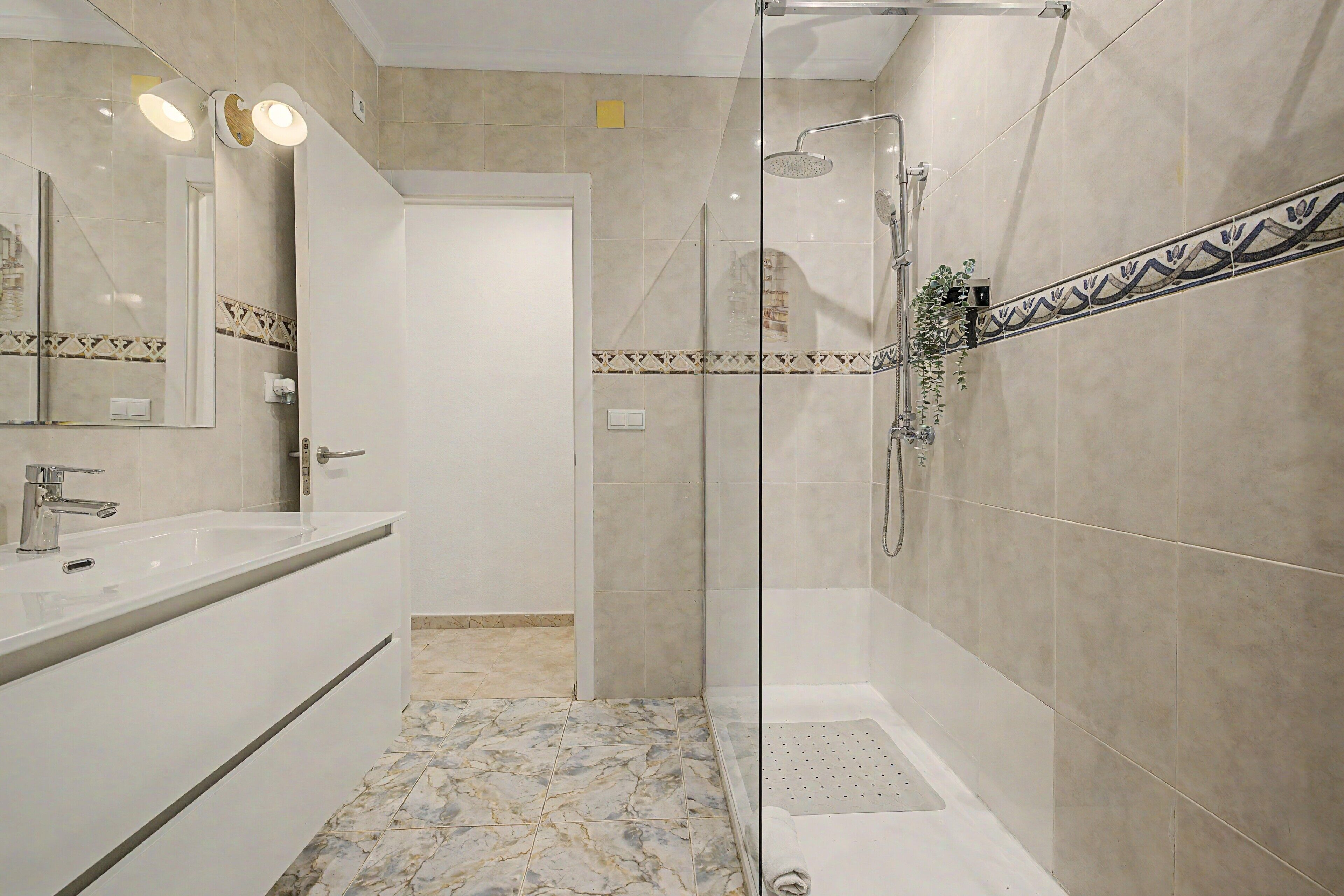 Une salle de bain moderne avec une douche à parois de verre, un lavabo blanc et un miroir avec éclairage intégré.