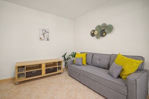 A living room with a grey sofa, yellow cushions, a wooden cabinet with drawers, a wall-mounted decorative piece, and a potted plant. - Apartment 'Sunandbed Sol' with Private Terrace, Balcony and Air Conditioning (Salou)