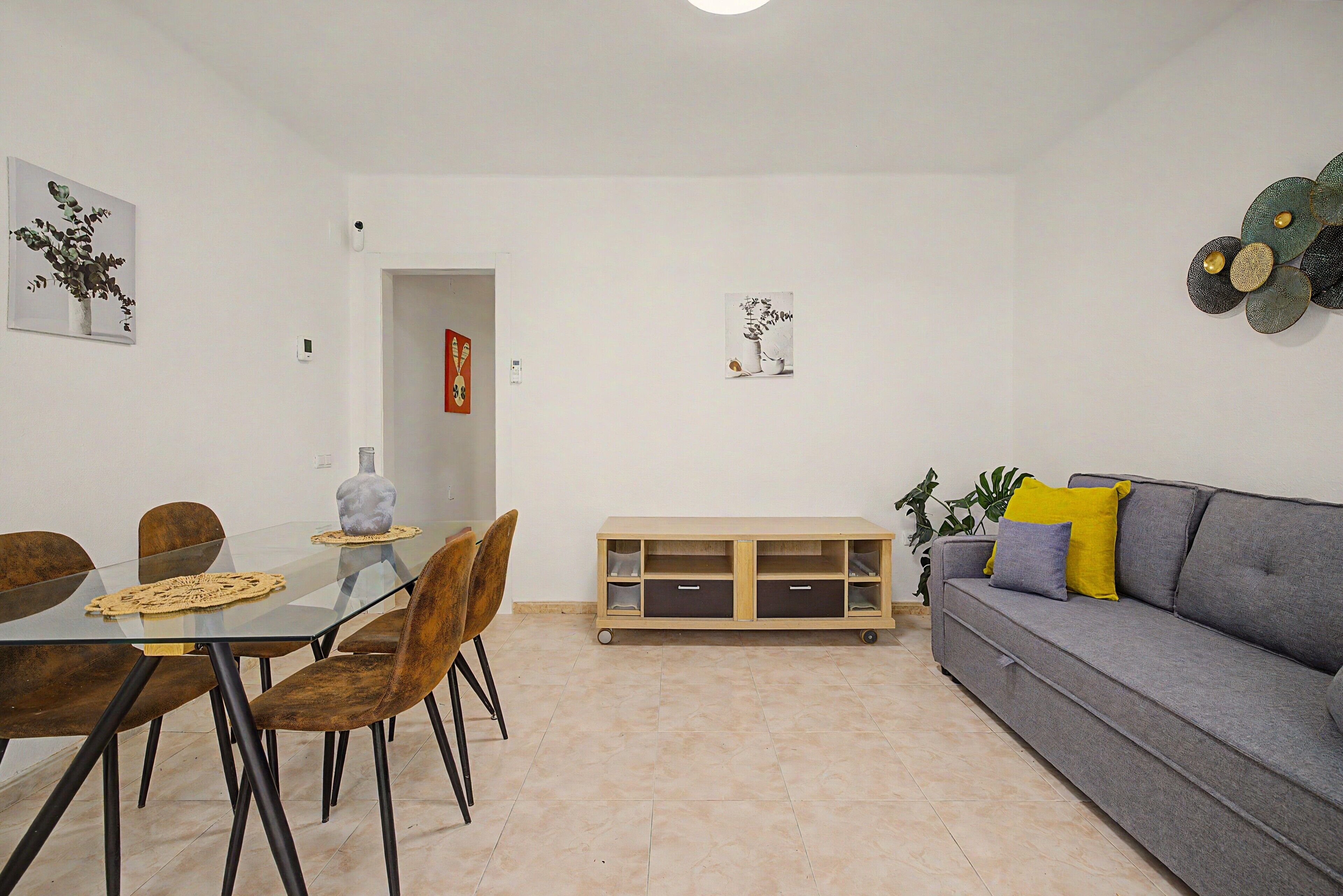 Una sala moderna con un sofá gris, una mesa de comedor con sillas y un mueble bajo.
