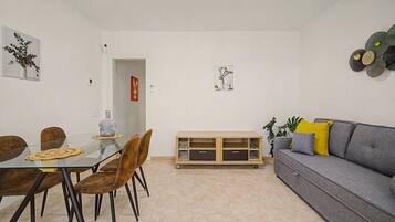 Una sala moderna con un sofá gris, una mesa de comedor con sillas y un mueble bajo.