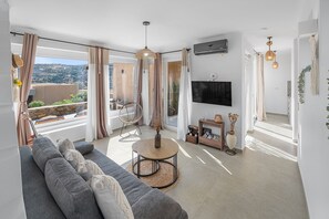 A modern living room with a grey sofa, a round coffee table, and a TV mounted on the wall. - The Aer Element Of Gaea (Loutra)