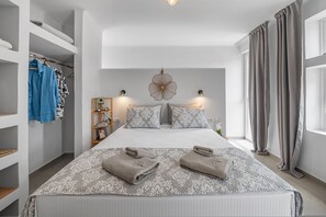 A hotel room with a large bed, a wardrobe, a vanity with a mirror, and a window with curtains. - The Aer Element Of Gaea (Loutra)