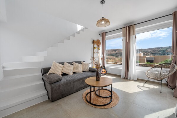 A modern living room with a grey sofa, a round coffee table, and a wicker chair.