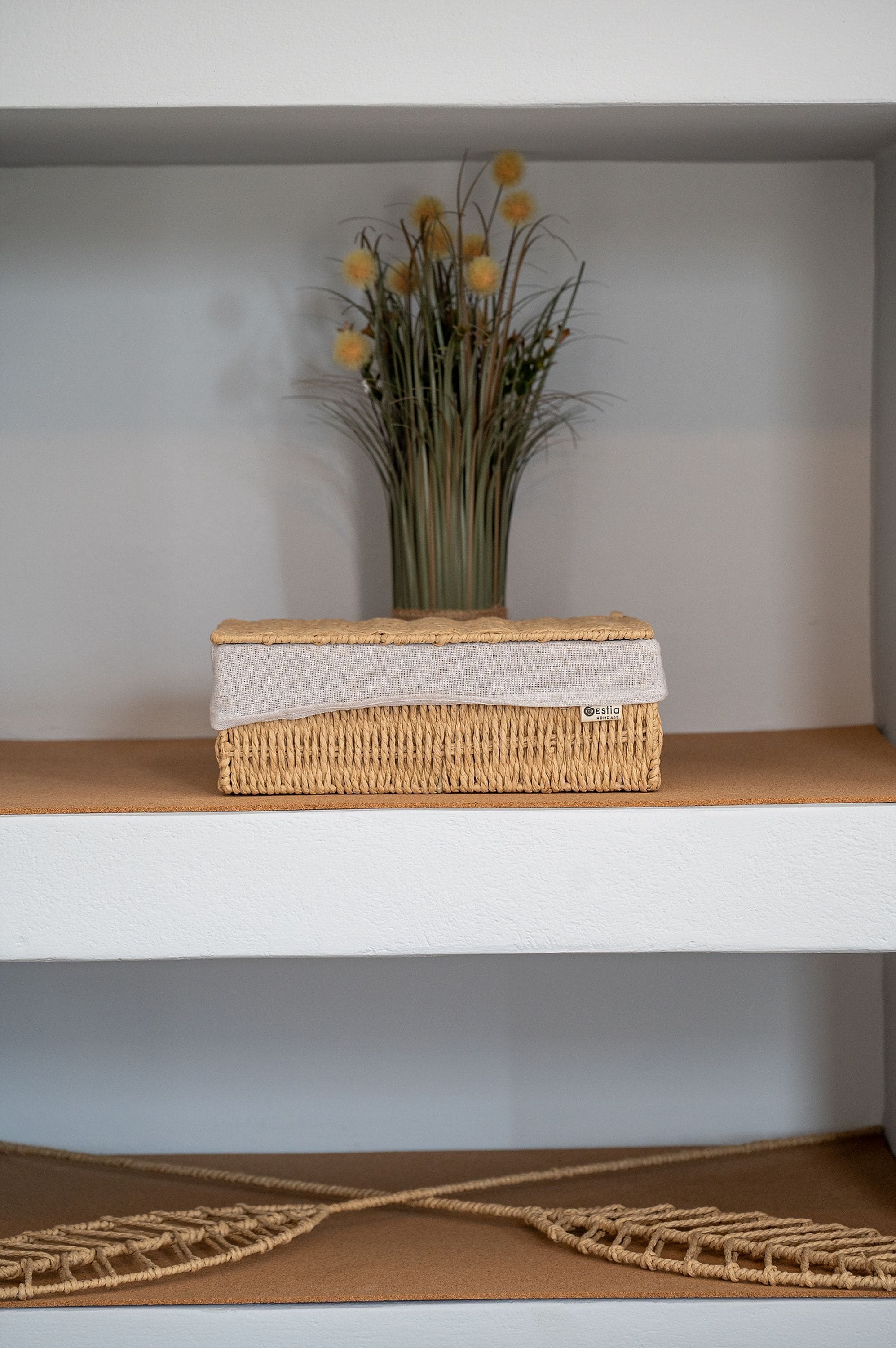 Een plank met een gevlochten mand en een vaas bloemen.