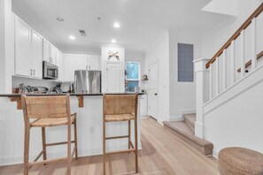 A modern kitchen with white cabinets, stainless steel appliances, and two wicker chairs. - BMR Heart & Home LLC (Charlotte)