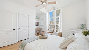 Ein Schlafzimmer mit Bett, Deckenventilator, Fenster mit Blick und Stuhl.