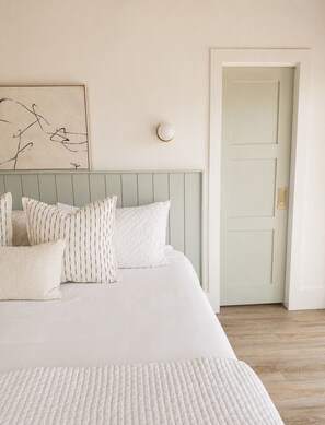 A bedroom with a bed, pillows, a wall-mounted light, and a door. - Canopy House - Walk to Harbour Town - Marshfront Oasis (Hilton Head Island)