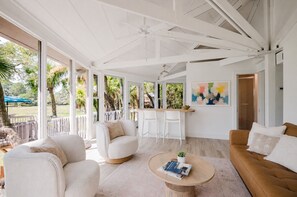 Uma sala de estar espaçosa com uma janela grande, um ventilador de teto e um espaço de refeições com um balcão.