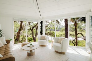A spacious room with large windows, a round coffee table, two white armchairs, and a brown sofa. - Canopy House - Walk to Harbour Town - Marshfront Oasis (Hilton Head Island)