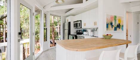 A modern kitchen with white cabinetry, a wooden island, and a large window overlooking greenery.