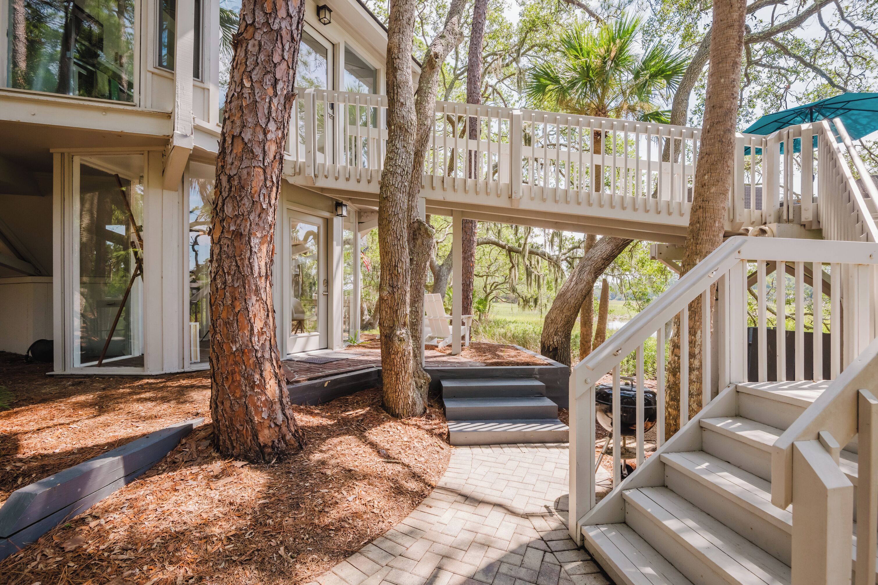 A multi-level outdoor deck with a staircase leading to a covered area, surrounded by trees and a brick pathway.