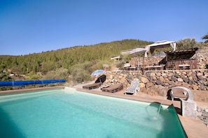 A pool area with lounge chairs, a stone wall, and a view of a forested hill. - Casa Dani: Tranquility in the Mountains with Pool and Garden (Cruz de Tea)